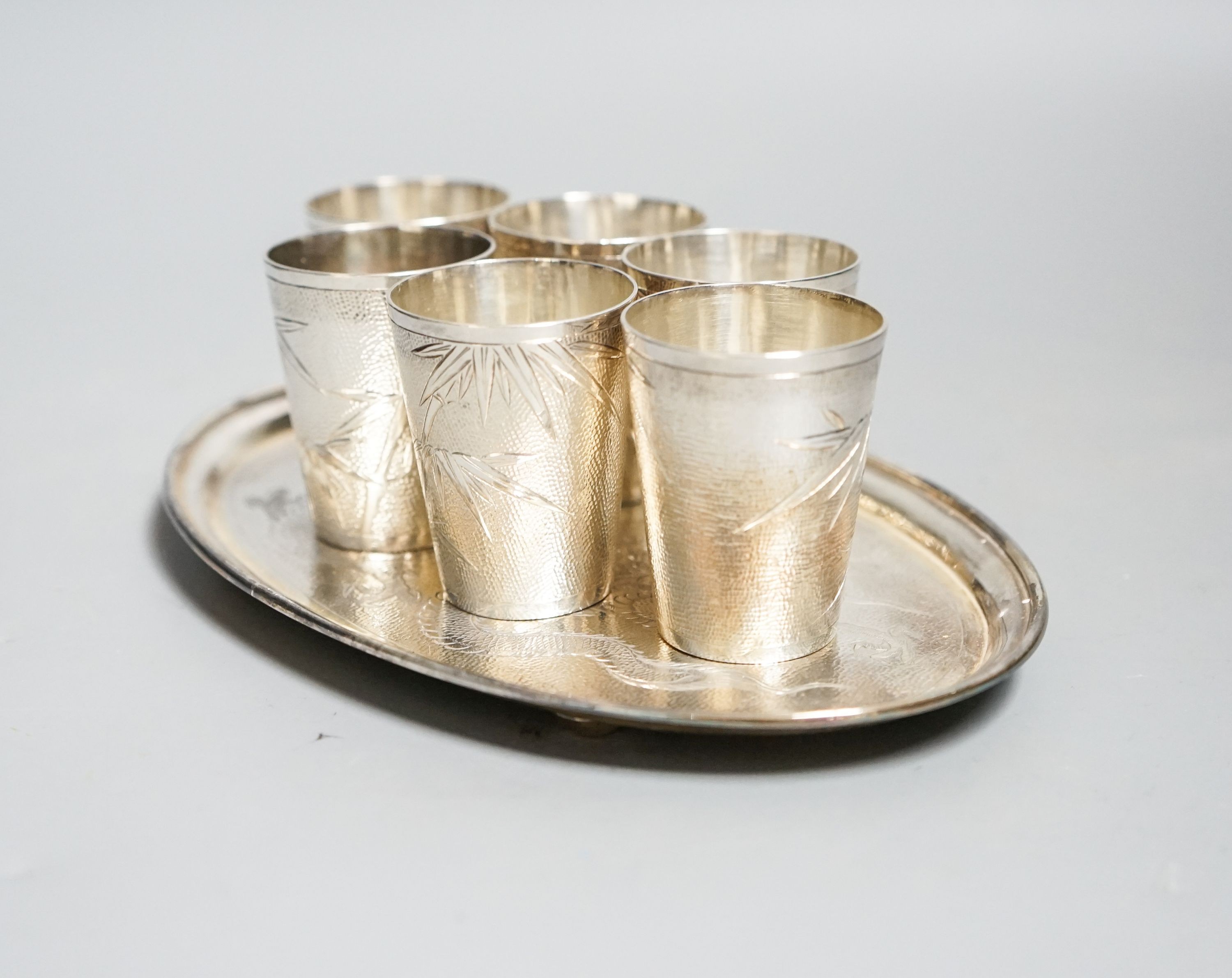 A set of six Chinese white metal tots by Tack Hing, 50mm and a small oval tray by Kingsburg, Hong Kong, 10.5oz.